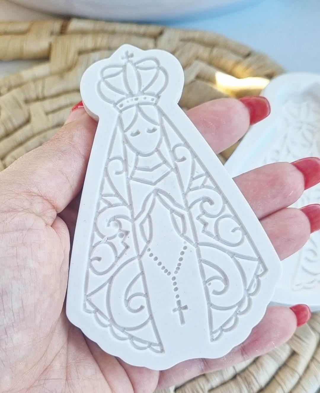 Molde branco em relevo com Nossa Senhora e cruz, segurado na mão