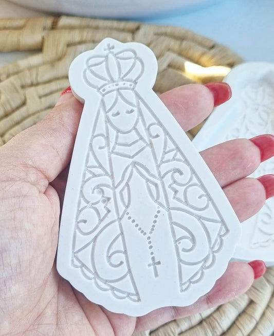 Molde branco em relevo com Nossa Senhora e cruz, segurado na mão