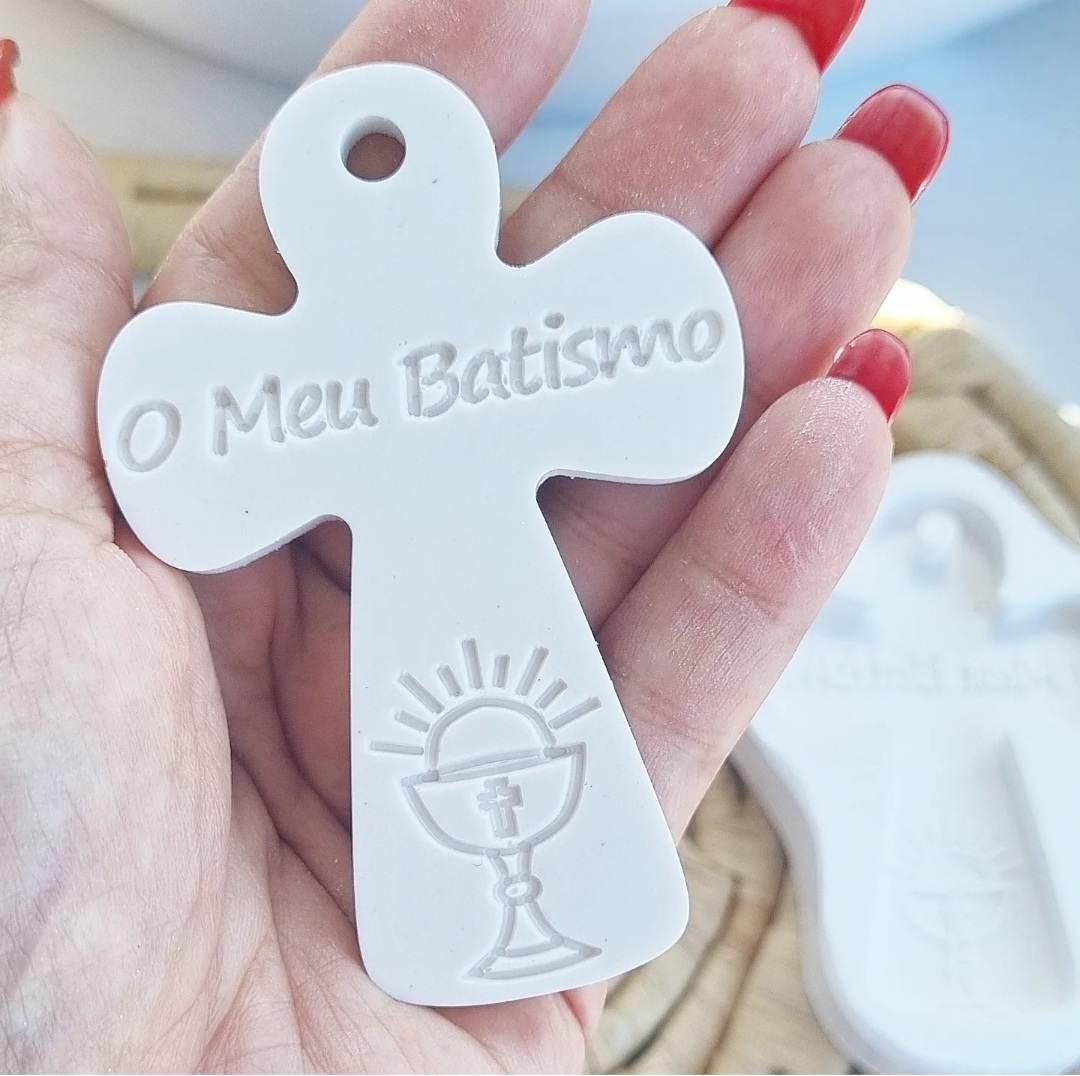 Molde de cruz branco em mãos, com “O Meu Batismo” e cálice gravados
