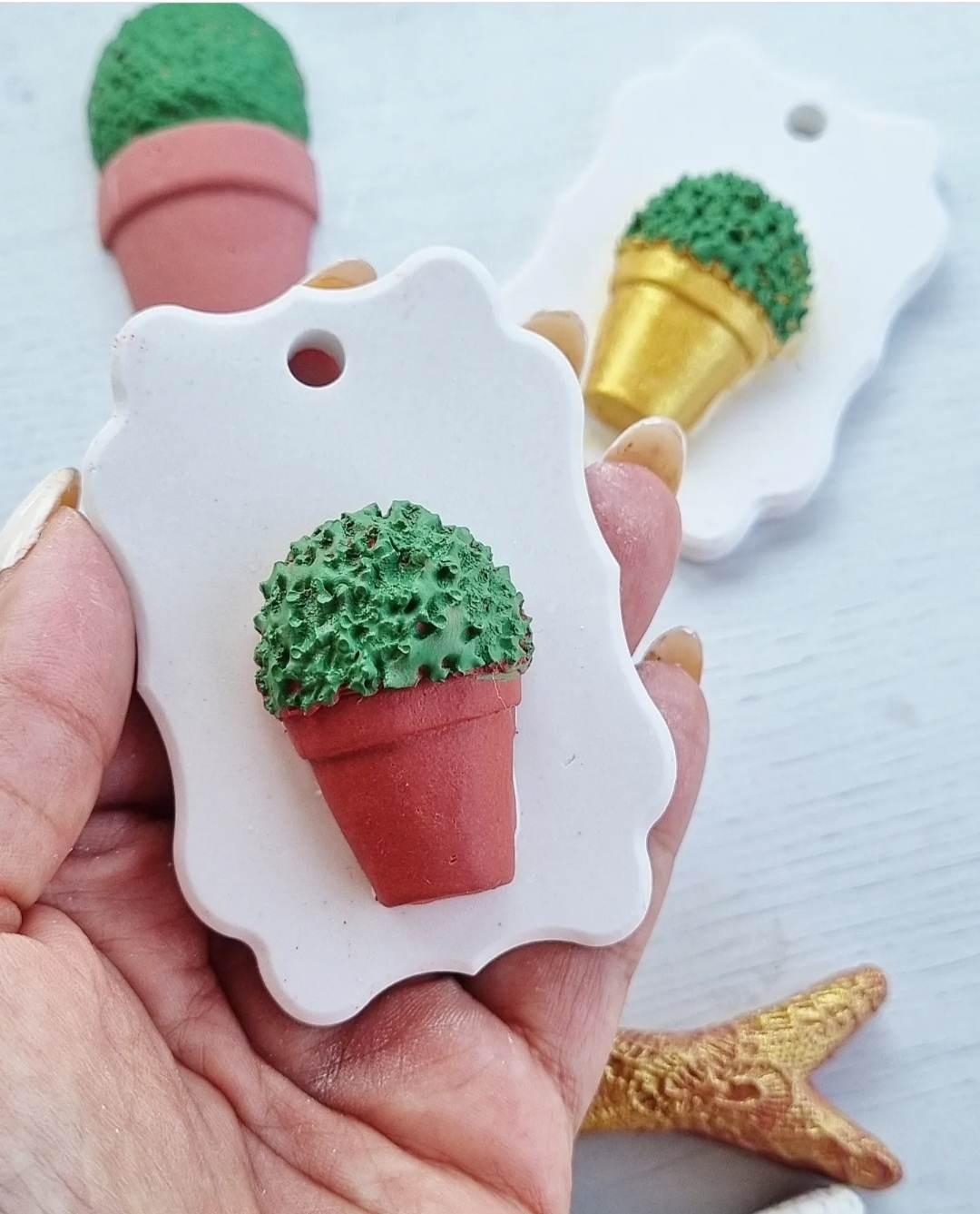 Molde branco em forma de flor com mini manjerico em vaso vermelho, segurado à mão