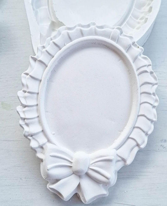 Molde de moldura oval branca com laço e frisos ondulados decorativos
