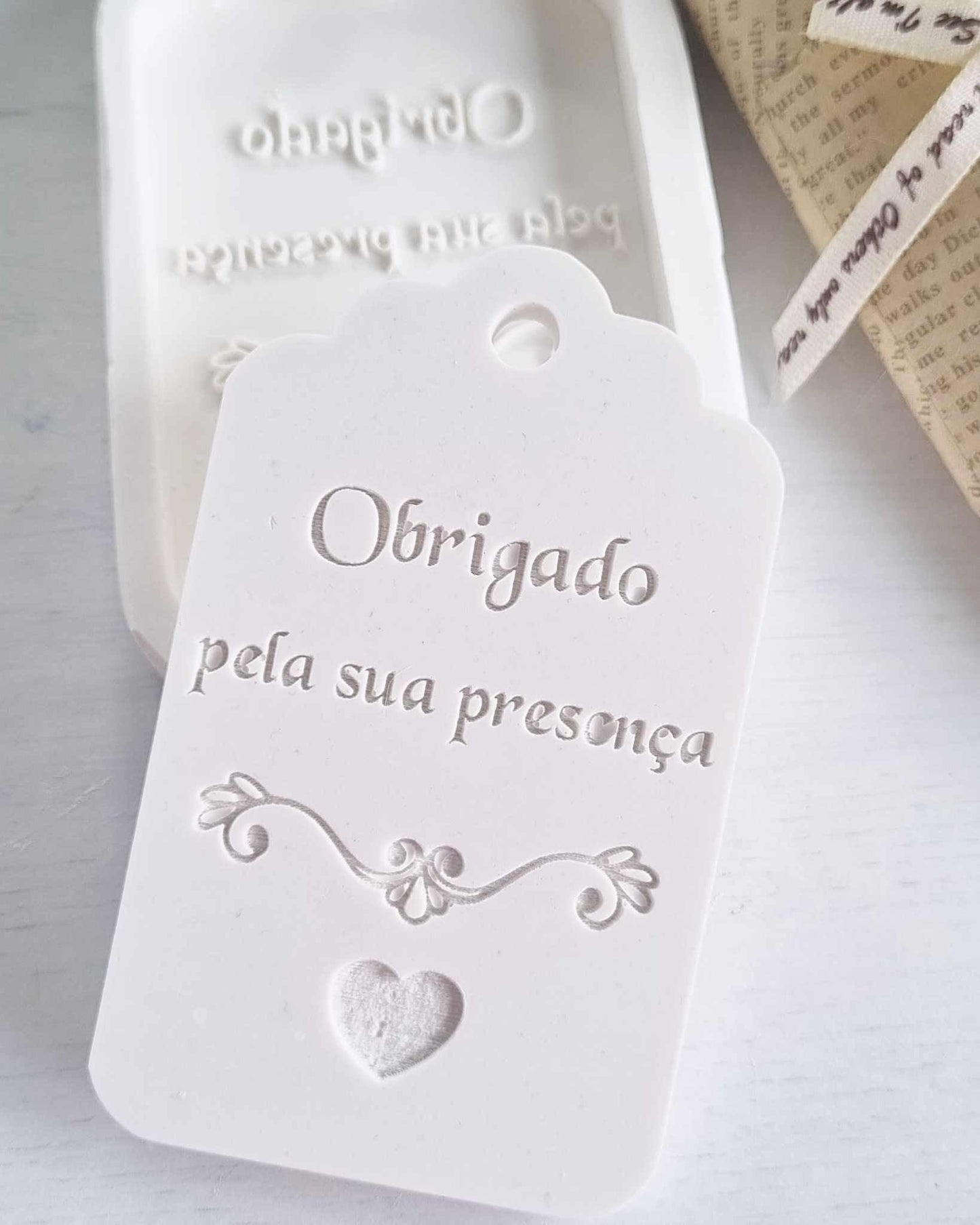 Molde/etiqueta decorativa branca com texto “Obrigada pela sua presença” e coração