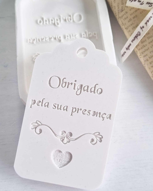 Molde/etiqueta decorativa branca com texto “Obrigada pela sua presença” e coração