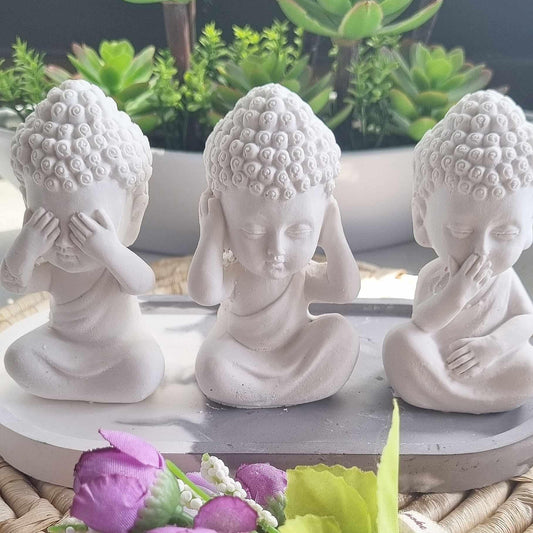 Três figuras de Buda sentadas brancas, mãos ao rosto, em bases redondas