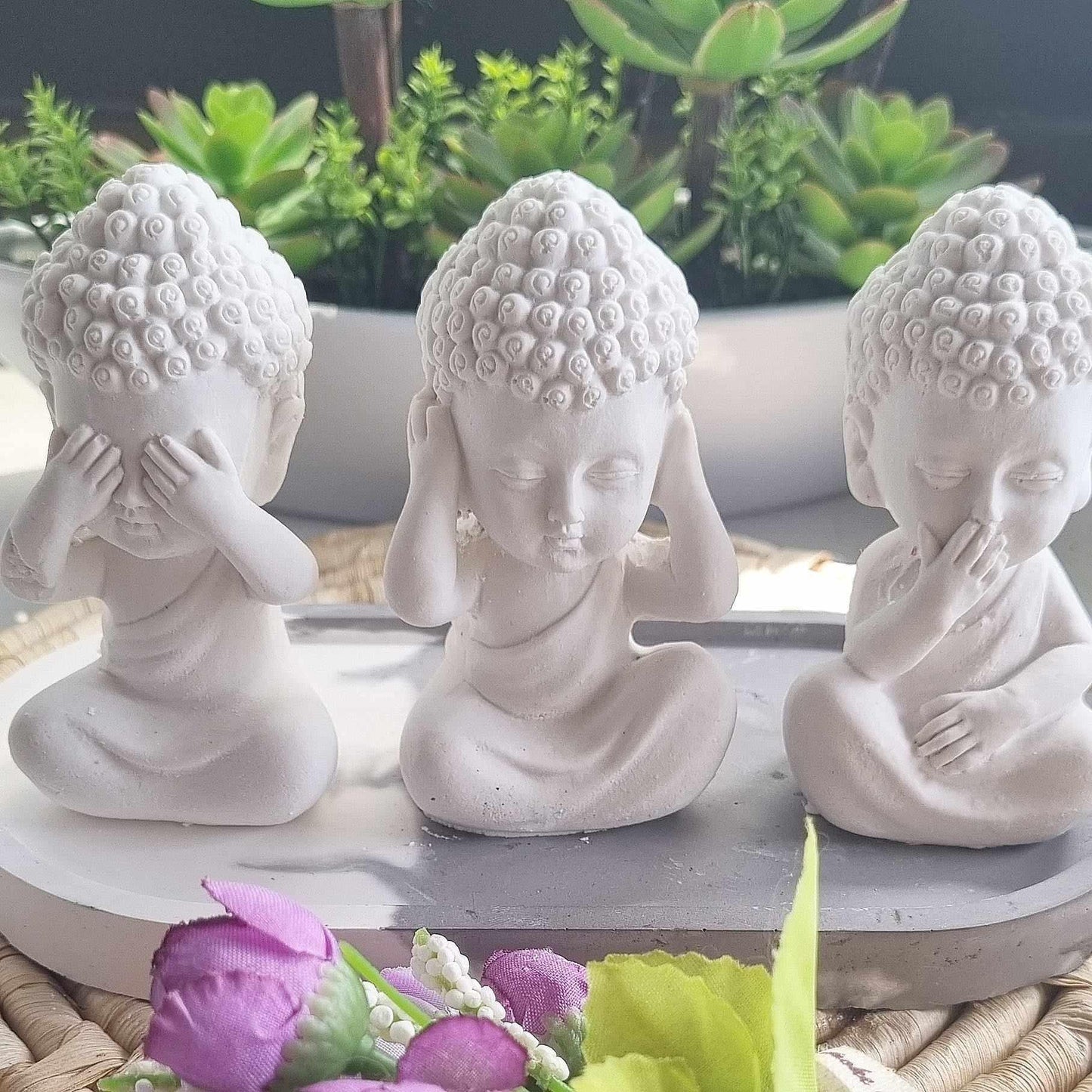 Três figuras de Buda sentadas brancas, mãos ao rosto, em bases redondas