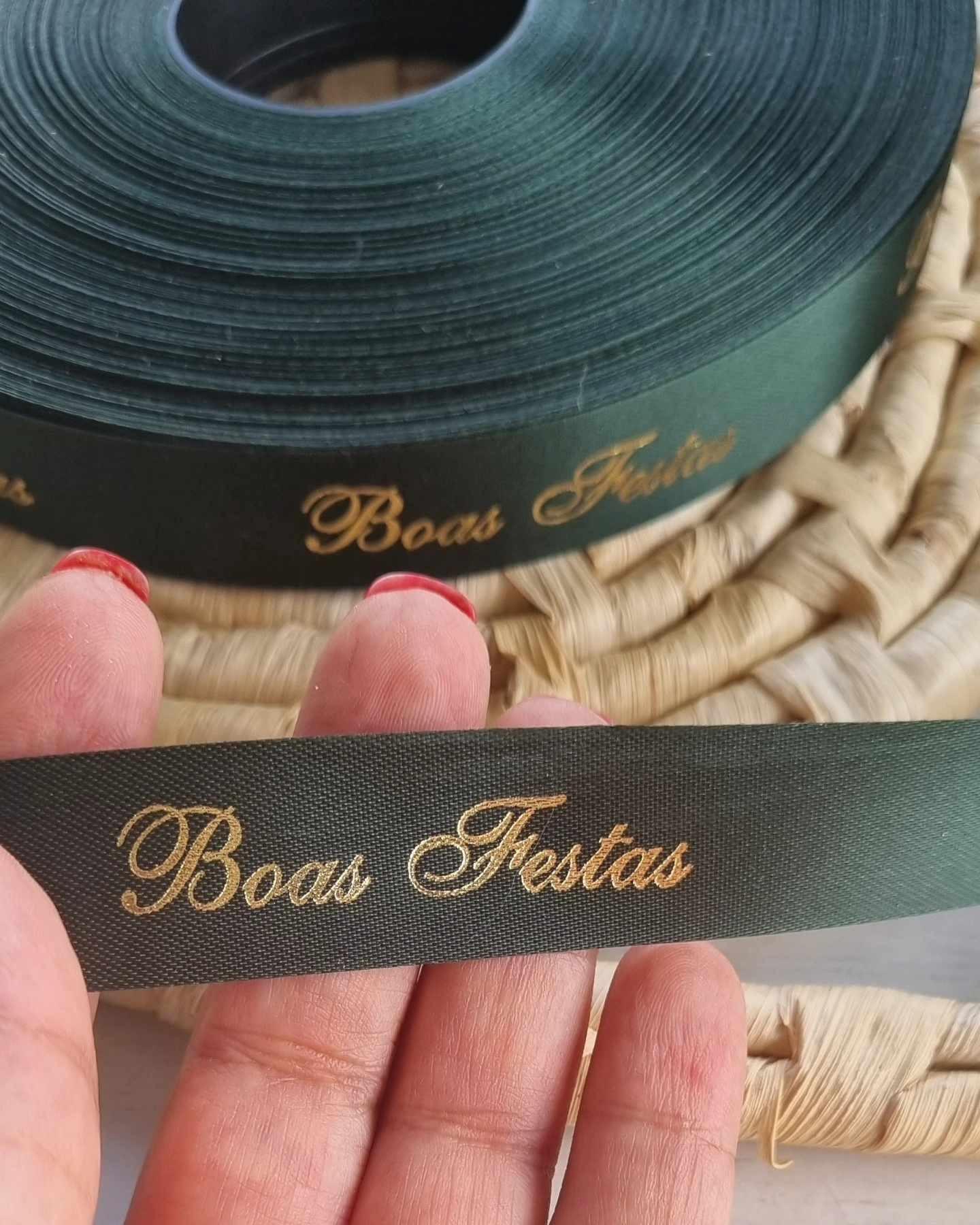 Fita verde-escura com “Boas Festas” em letras douradas, segurada com a mão