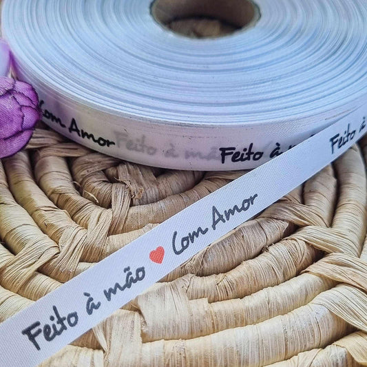 Fita branca de tecido com texto “Feito à mão” e “Com Amor” com corações vermelhos