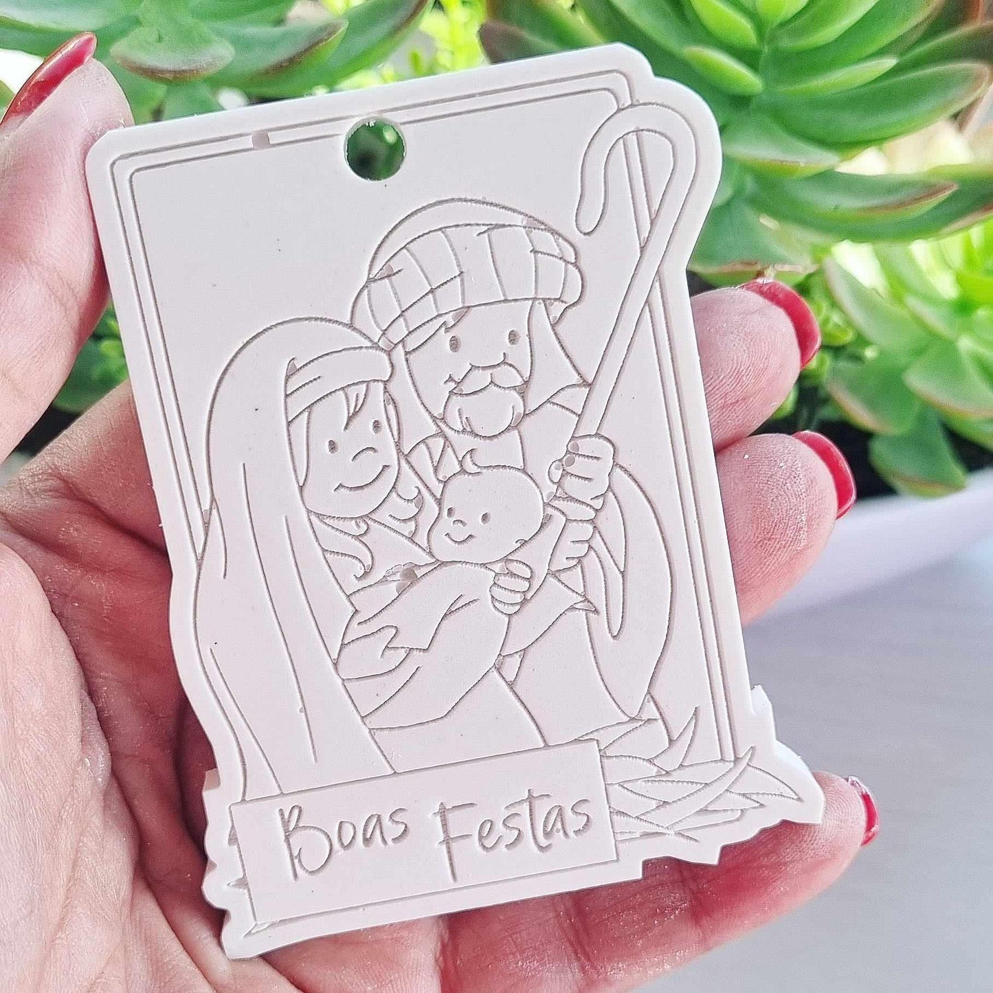 Molde de presépio branco com furo, relevo de figuras e texto 'Boas Festas'.