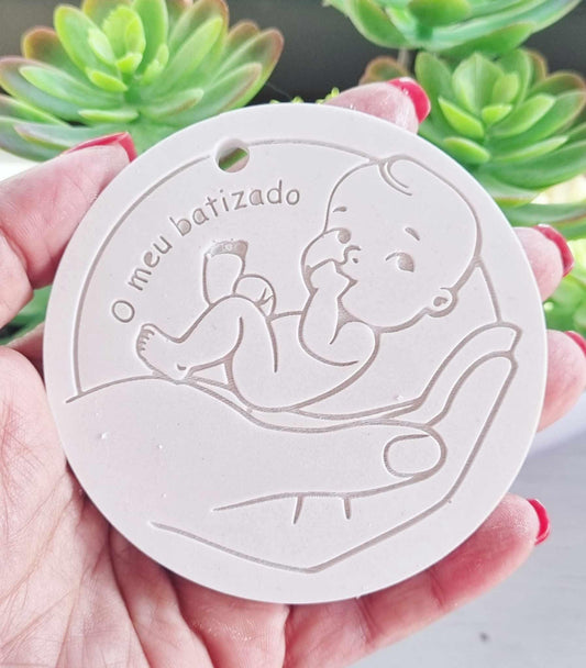 Molde redondo branco de batizado com relevo do bebé e texto “O meu batizado”, na mão.