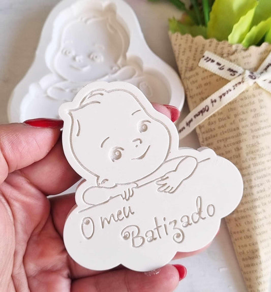 Molde de bebé branco em relevo, segurado na mão, com “O meu Batizado”
