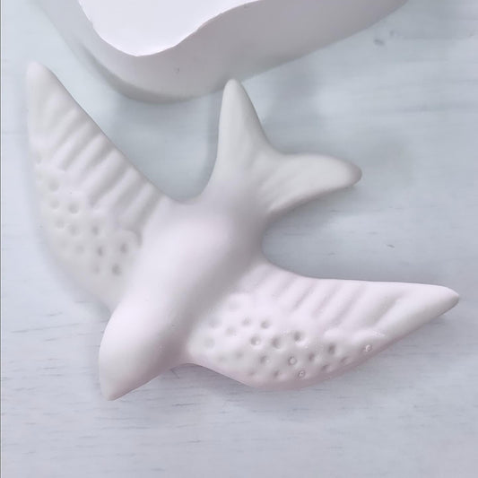 Molde em forma de andorinha branco, com relevo e pequenos pontos na superfície