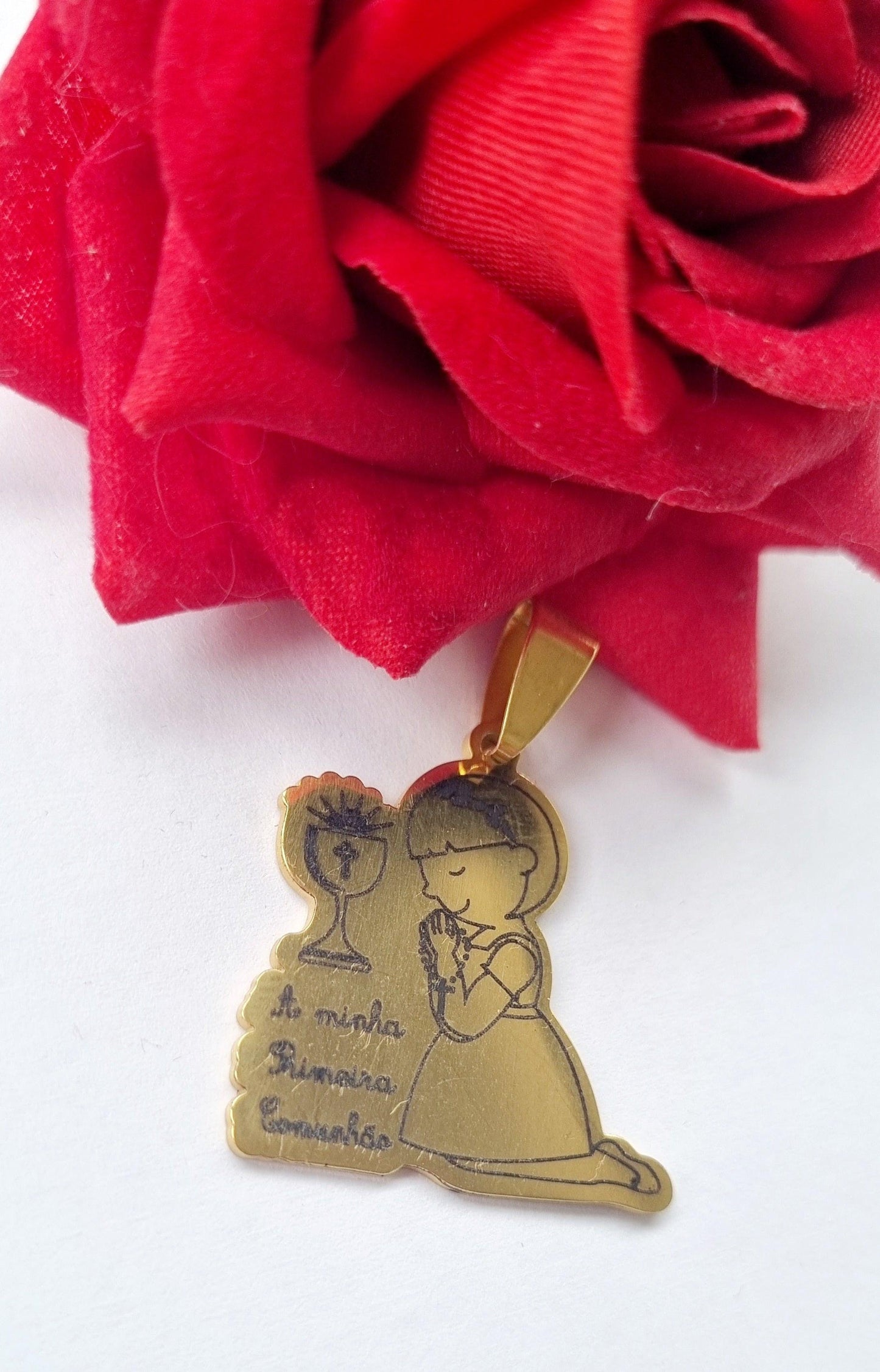 Medalha dourada de primeira comunhão com menina ajoelhada, cálice e texto