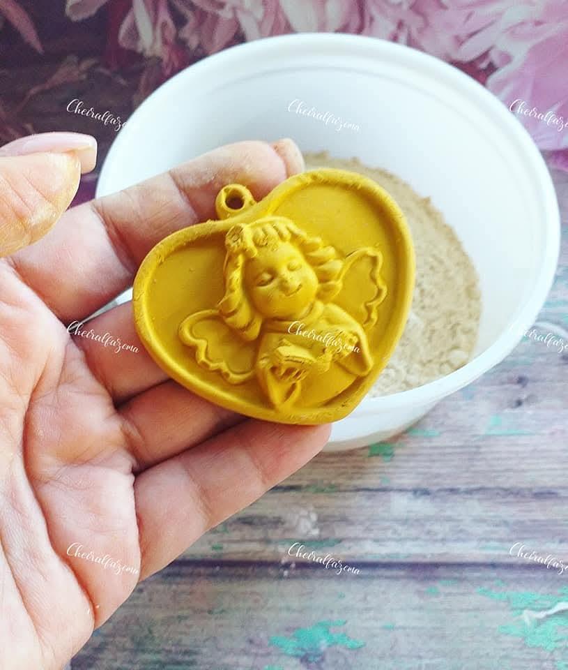 Medalhão de gesso amarelo com relevo de anjo, segurado na mão