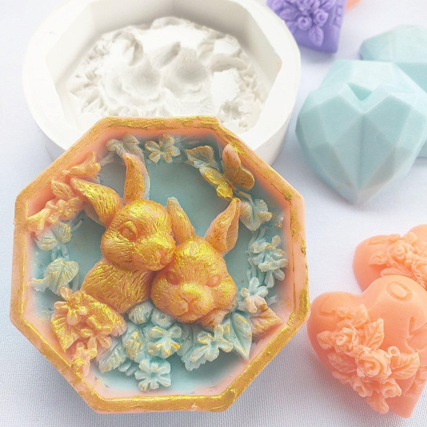 Molde de coelhos em silicone azul, com coelho dourado e flores azul-claro em relevo