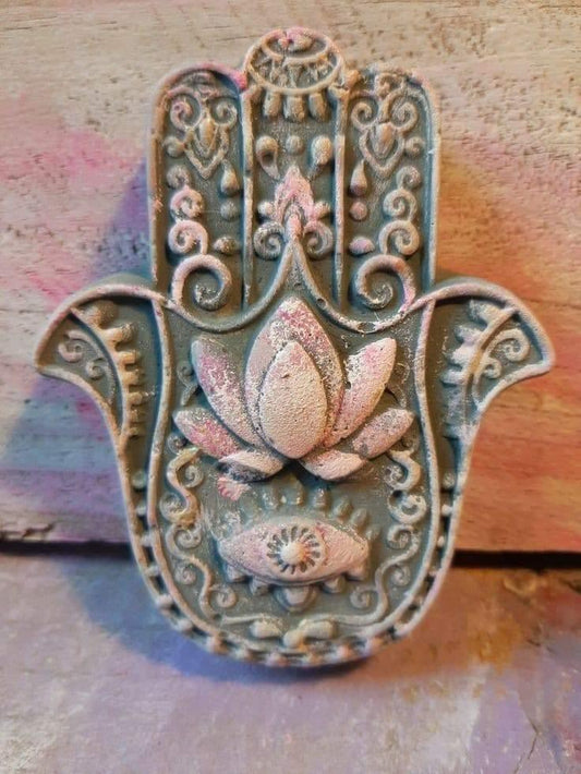 Mão de Fátima decorativa em resina azul-esverdeada, com detalhes rosa e dourados