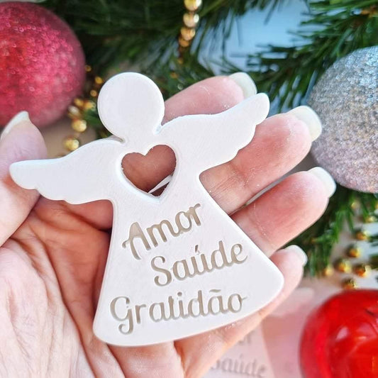 Molde de anjo branco na mão, com coração e inscrições “Amor Saúde Gratidão”