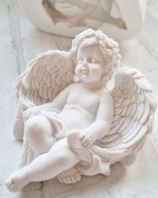 Figura de anjo em relevo com asas abertas, criança sentada e braços cruzados