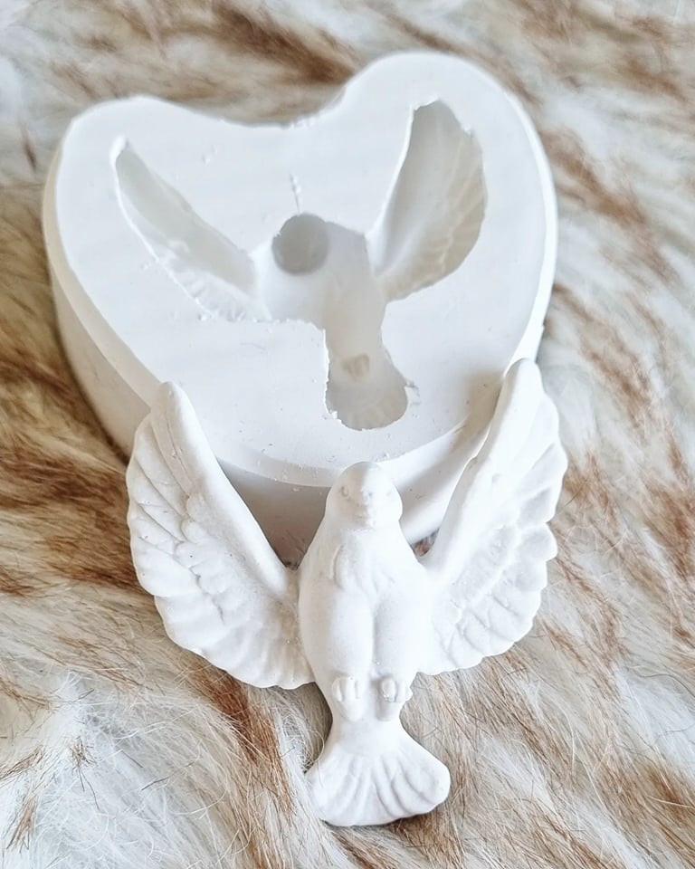 Molde em forma de pomba do Espírito Santo, com relevo branco e asas abertas.