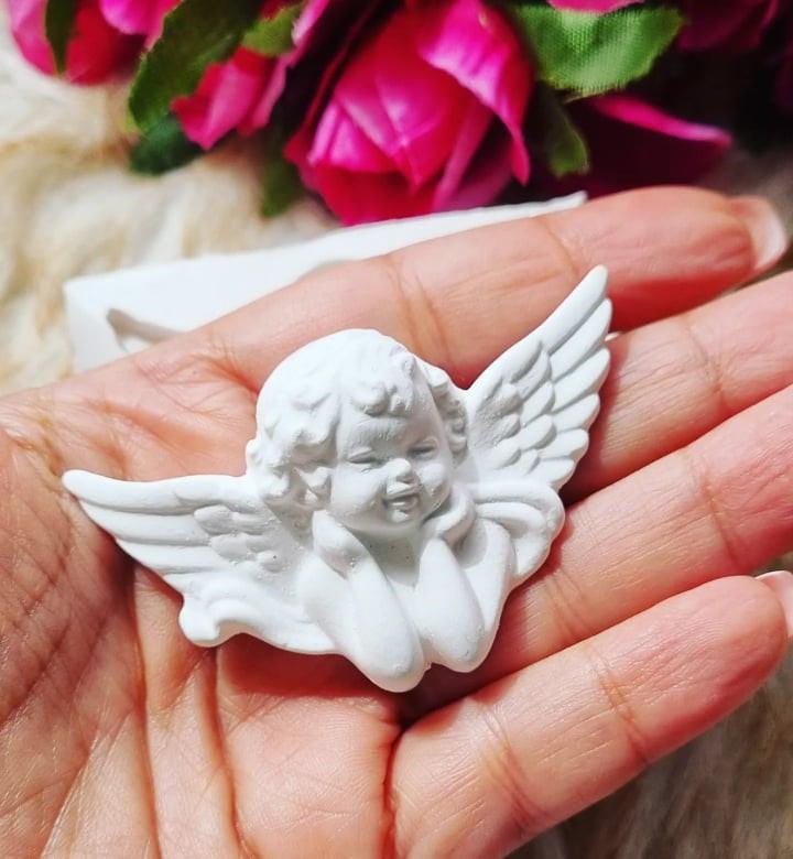 Anjo decorativo branco em relevo com asas abertas, visto na palma da mão