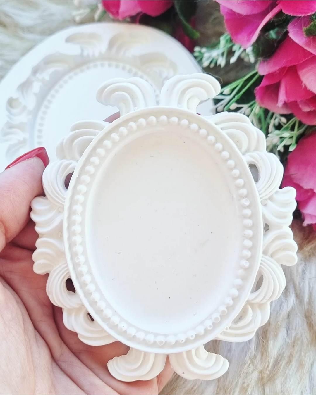 Molde de moldura oval pequena branca com aro perolado e ornatos florais, segurado na mão