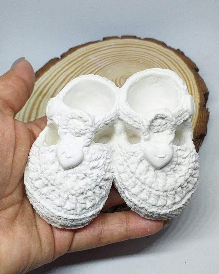 Botinhas de bebé em crochet branco, vistas de cima, com rostos