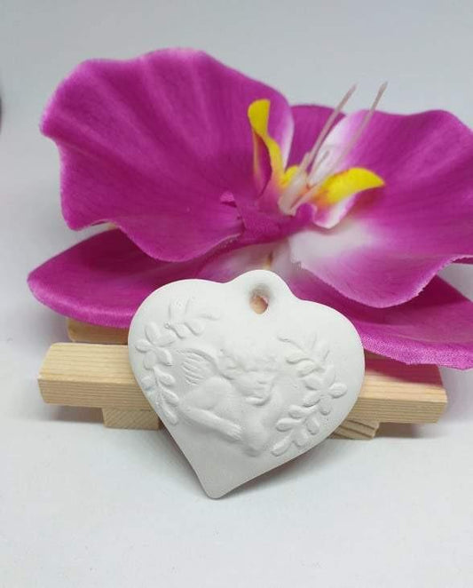 Molde de coração branco com relevo de anjo e motivos florais, sobre base de madeira