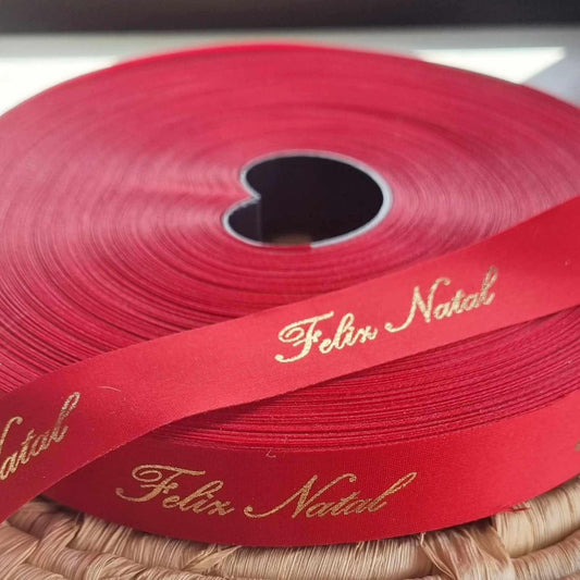 Fita vermelha com letras douradas “Feliz Natal”, enrolada em rolo