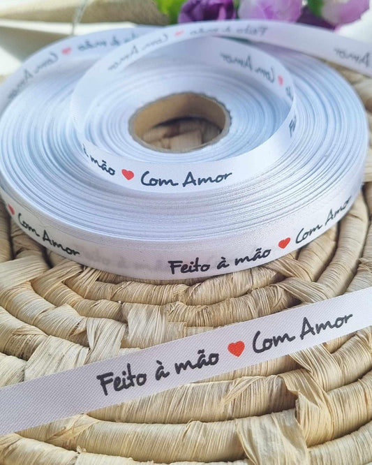 Fita branca de tecido enrolada, com impressão “Feito à mão” e corações vermelhos